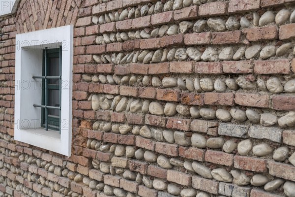 Oblique view of a wall made of bricks and river stones with a green window