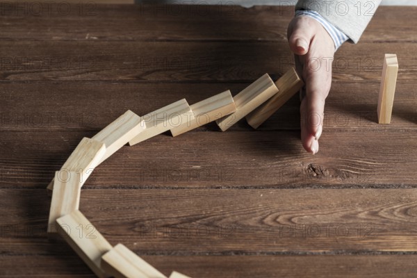 Businesswoman protecting dominoes from falling on wooden desk. Business assistance and leadership in crisis. Operative business solution and stabilization of situation. Professional risk management