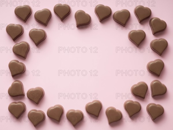 Frame of romantic chocolate confections in heart shapes on pastel pink background. Canvas with heart chocolate sweets with copy space. Valentines day background