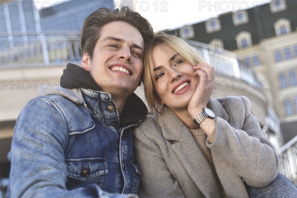 Attractive young couple sitting on floor in urban street reading information on a tablet with a smile