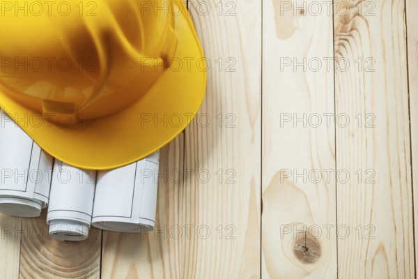 Yellow construction helmet and white rolled blueprints on wooden boards