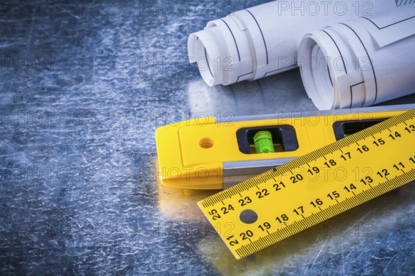 Rolled up blueprints ruler and construction level on metallic scratched background maintenance concept