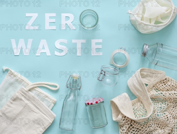 Zero waste concept. Textile eco bags, glass jar and bottle on blue background with Zero Waste white paper text. Eco friendly and reuse concept. Top view or flat lay