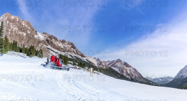 A sunny day of winter on the snowy pastures and the rocky peaks of the Austrian Alps mountains, with the roads being cleared by a snow groomer vehicle