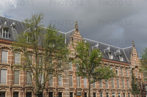 Historic buildings with gables and trees, cloudy sky, Amsterdam, Netherlands