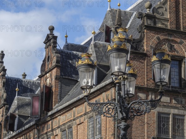 Historic building with ornate roof edges, in the foreground a decorative lantern under a slightly cloudy sky, nijmegen, netherlands