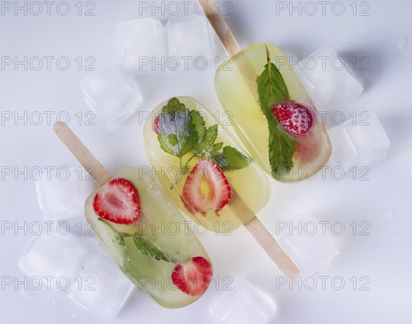 Popsicles with lemon balm and strawberries and ice cubes on a white background