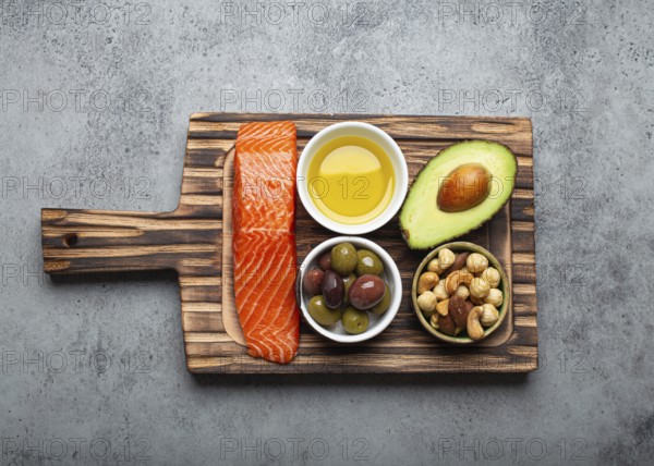 Food sources of healthy unsaturated fat: fresh raw salmon fillet, avocado, olives, nuts on cutting board on rustic stone background top view. Omega 3 and oil products, healthy nutrition and keto diet, food photography, food photography