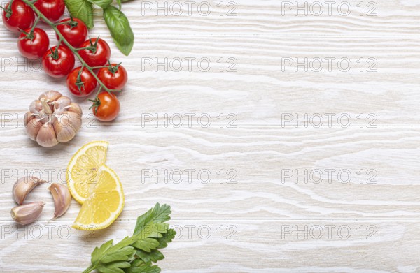 Healthy food ingredients composition with fresh cherry tomatoes, herbs, garlic cloves, lemon wedges on white wooden rustic background, overhead shot with copy space, food photography, food photography