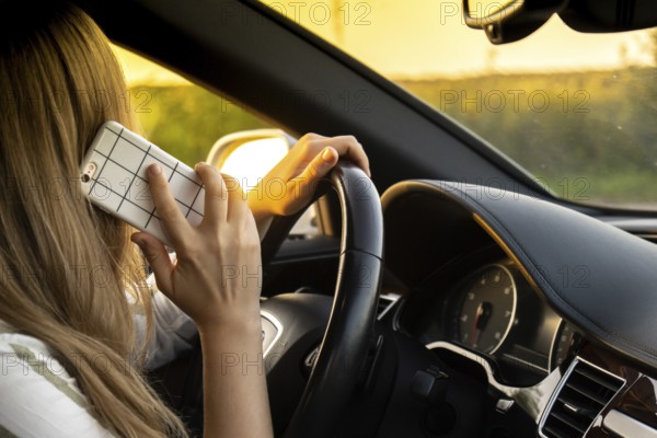 Young woman using mobile phone while driving car on highway road during sunset. Womandriver has accident calling with smartphone for help. Business woman busy driving concept