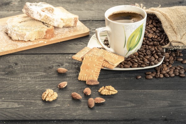 Healthy snack with slices of pound cake, biscuits, almonds, walnuts and a cup of coffee on a plate covered with coffee beans