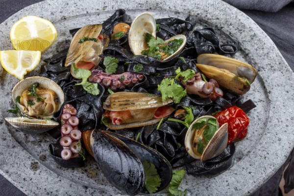 Food, Seafood black fettuccine fehttuchini. Black pasta with squids, octopus clams, mussels on stone plate. Gourmet dish