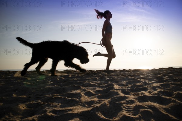 Girl running in the company of her dog on the seashore shot against the light