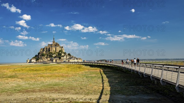 Mont Saint-Michel in summer with a pedestrian bridge in the foreground and blue sky, Mont Saint Michel in Normandy, France