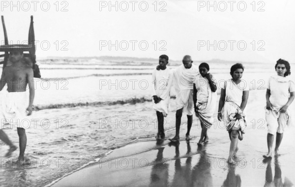 Mahatma Gandhi and others walking Juhu Beach, Mumbai, May 1944, Kanu Gandhi, carrying a chair on his head, Sushila Nayar, India NO MR