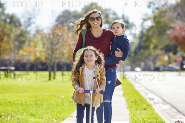 Mother daughter and son family in the park walking with ball and skate scooter