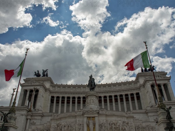 Monumental building with two Italian flags and equestrian statue under a cloudy sky, Rome, Italy