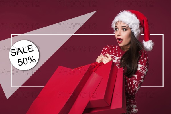 Christmas woman. Beauty model girl in santa hat on red background. Funny laughing surprised woman portrait. Open mouth. True emotions. Red lips and beautiful holiday makeup. Shopping and sale. Shopaholic girl. Black Friday, holiday celebration