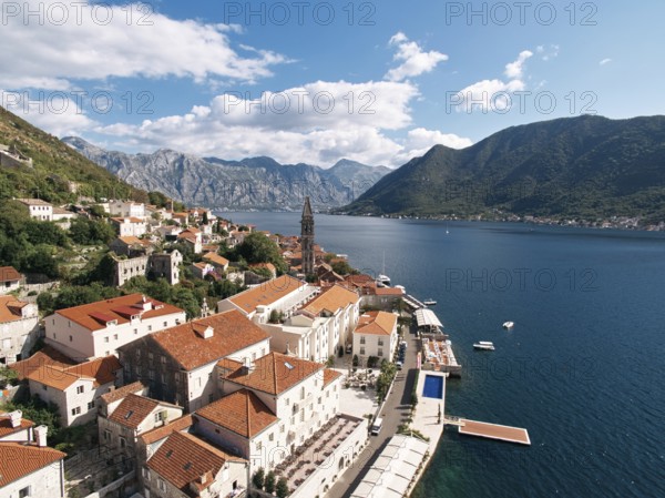 Old houses with red roofs on the shore of the Bay of Kotor with a swimming pool on the promenade. Perast, Montenegro. Drone.