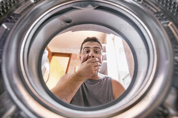 Shocked upset Young man Looking At Stained Bleached Cloth In Washing Machine. View from the inside of washing machine