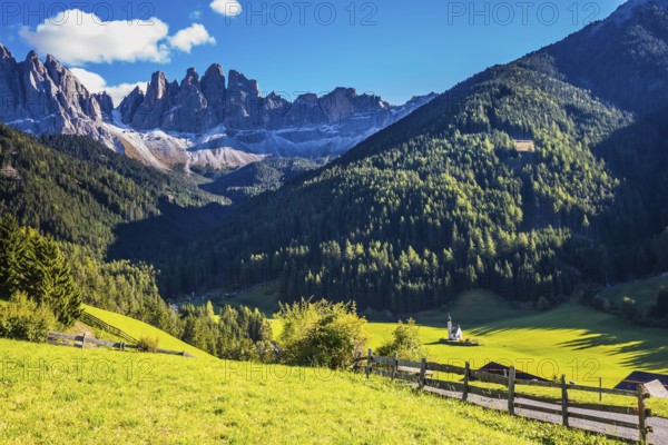 Picturesque little church of Santa Maddalena in valley Val di Funes. Sunny day in Dolomites, Tirol. Rocky peaks and forested mountains surrounded by green Alpine meadows