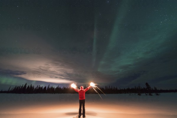Man with burning sparklers and Northern Lights (Aurora borealis), Muddus National Park, Laponia World Heritage Site, Norrbotten, Lapland, Sweden, December 2016