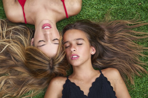 Teenager best friends girls lying down on backyard turf grass