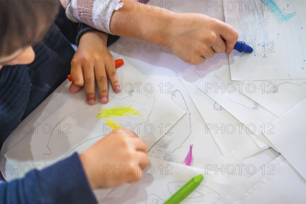 Two kids coloring drawings of animals with wax crayons, developing their creativity and fine motor skills