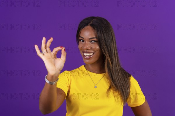 Studio portrait with purple background of an african smiling urban woman gesturing agreement with hand