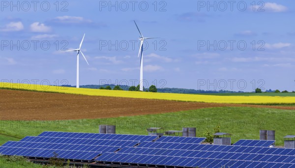 Landscape of the Swabian Alb in spring with rape field and wind turbines. In front of it a building with photovoltaic collectors. Dornstadt Baden-Württemberg, Germany