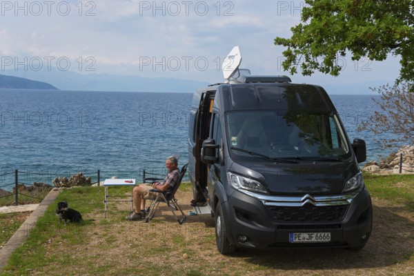 A campsite by the sea, a man sits next to a motorhome and enjoys the view with a dog, Glavotok, Krk island, Primorje-Gorski kotar, Croatia