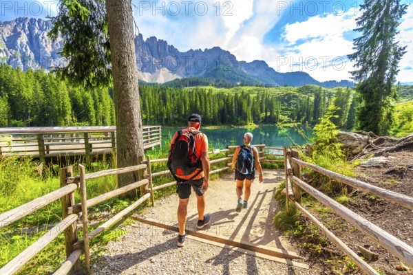 Tourists walking on a path towards the turquoise waters of lake carezza, surrounded by the stunning peaks of the dolomites, italy