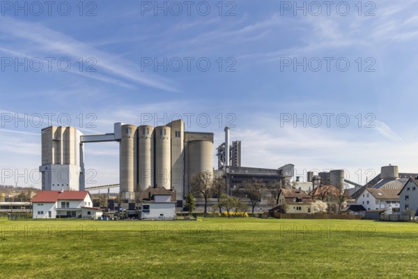 SCHWENK cement works in Heidenheim-Mergelstetten. In front, residential buildings with an idyllic garden as a contrast to the concrete towers. Heidenheim, Baden-Württemberg, Germany