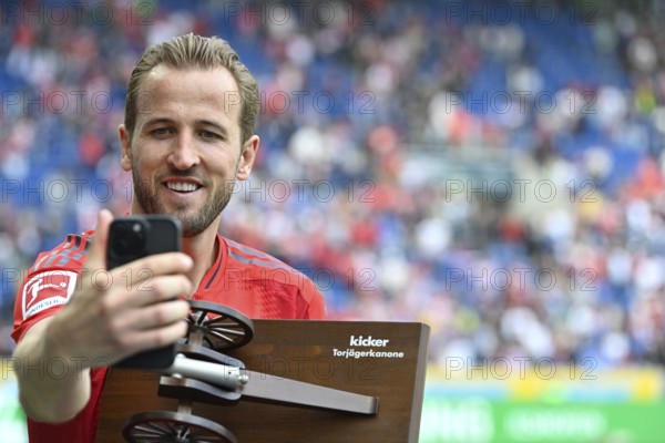 Harry Kane FC Bayern Munich FCB (09) smiles, proudly takes selfie with smartphone of his goal scorer's crown, honour, trophy, of the magazine Kicker Deutschland, PreZero Arena, Sinsheim, Baden-Württemberg, Germany