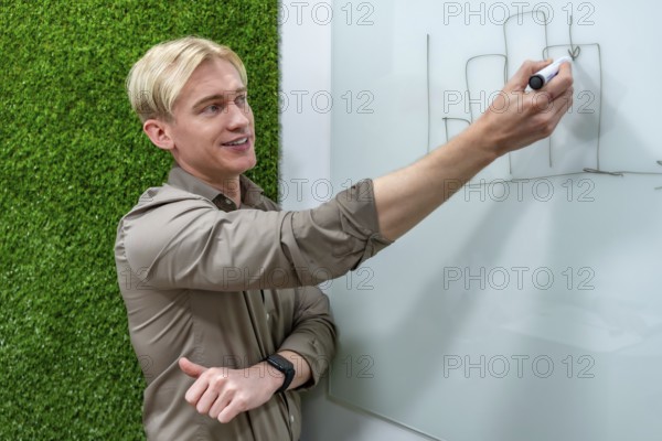 Young businessman drawing growing bar chart on whiteboard during a presentation in a modern office with a green wall