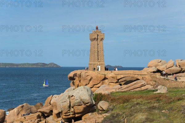 Lighthouse overlooking the rocky coast with sailing boat on the horizon, Phare de Men Ruz, Ploumanac'h, Ploumanach, Pointe de Squewel, Perros-Guirec, pink granite coast, Côte de Granit Rose, Brittany, France