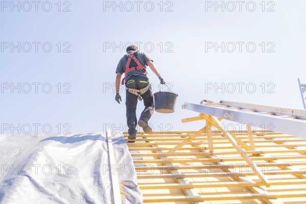 A worker in safety clothing climbs a ladder to work on a roof, in sunny weather, roof renovation, house construction, Pforzheim, Germany