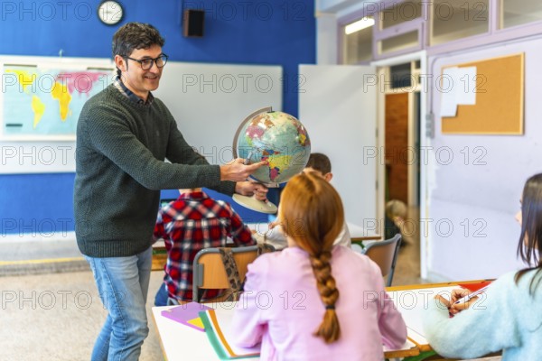 Geography teacher pointing a location on the globe to a classroom of elementary school students during a geography lesson