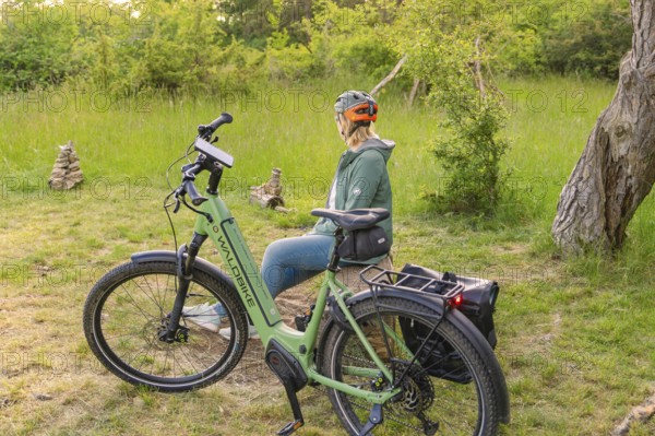 Cyclist with helmet sitting next to a bicycle, surrounded by green nature and trees, e-bike excursion, Gechingen, district of Calw, Germany