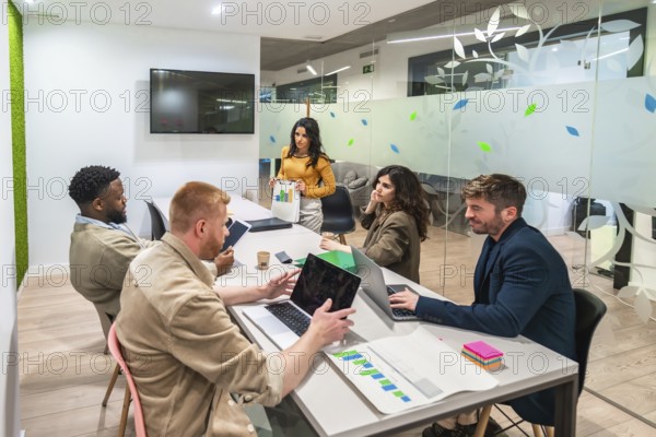Marketing managers collaborating on a project, analyzing charts and using laptops in a modern meeting room