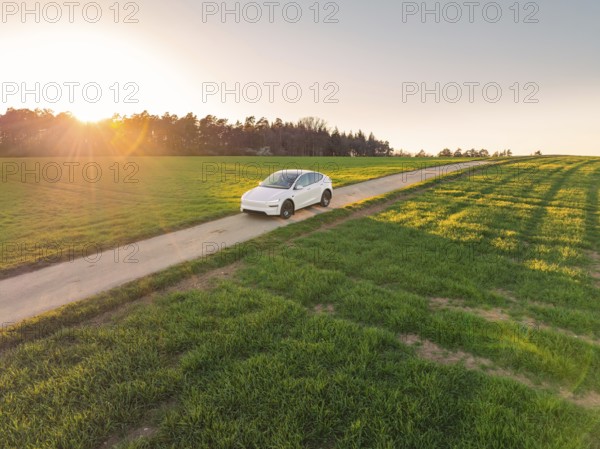 White electric car driving through a wide landscape on a country road at sunrise, Tesla New Model Y, Germany