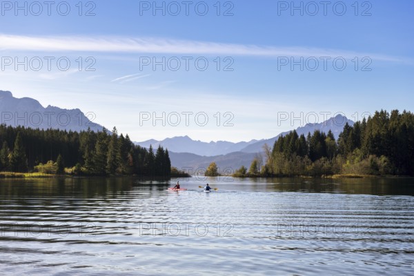 Two kayaks on a calm lake, framed by mountains and dense forests under a clear blue sky, Forggensee, Ostallgäu, Allgäu, Bavaria, Germany