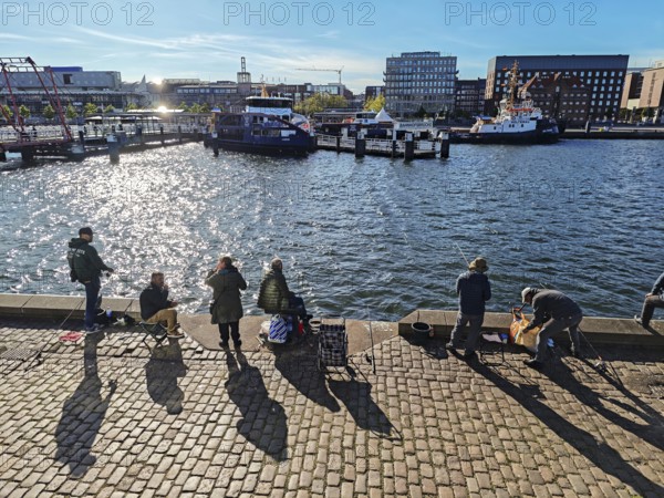 Kiel harbour at the end of the Kiel Fjord, view from the eastern shore with anglers to the western shore with the main railway station, Hörnbrücke bridge connects parts of the city, the pedestrian and bicycle bridge is a rare three-span folding bridge, technology, liner Laboe at the pier, tugboat, Atlantic Hotel, maritime atmosphere, backlight, blue sky and sunshine, Baltic Sea, Kiel, Schleswig-Holstein, Germany