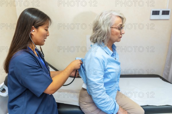 Female doctor examining the lungs of a senior woman with a stethoscope during a routine medical exam in a clinic setting
