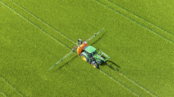 Farmer with tractor working in the field. In early summer, he fertilises the grain for an optimum yield. Drone photo. Merklingen, Baden-Württemberg, Germany