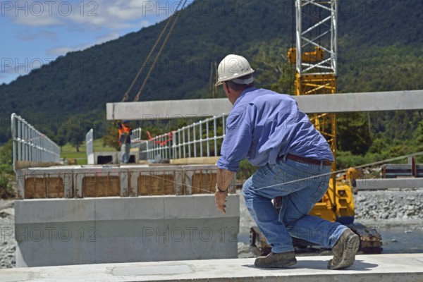Builders construct a concrete bridge over a small river in Westland, New Zealand