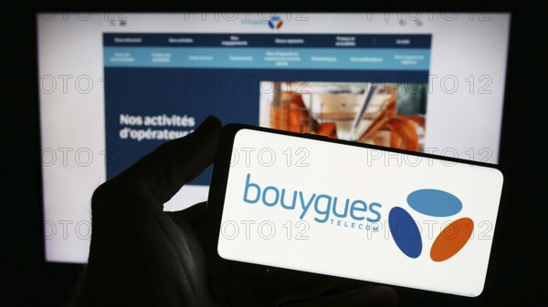 Stuttgart, Germany, 11-22-2023: Person holding smartphone with logo of French telecommunications company Bouygues Telecom S.A. in front of website. Focus on phone display