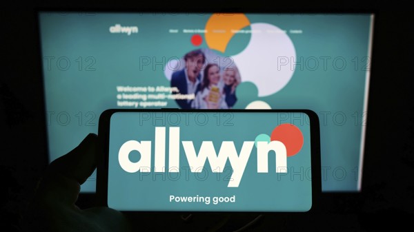 Stuttgart, Germany, 01-22-2022: Person holding mobile phone with logo of company SAZKA Entertainment AG (Allwyn) on screen in front of business web page. Focus on phone display