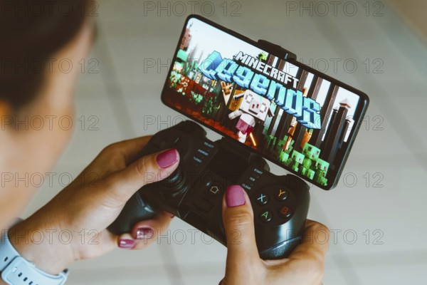 In this photo illustration, the Minecraft Legends logo is displayed on a smartphone screen as a person plays on a gaming gamepad