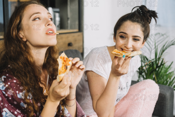 Two young women eating pizza home